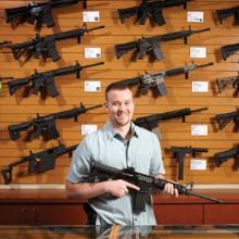 A Scottsdale Gun Club employee poses with a selection of firearms for sale. phm1212 gu2 md