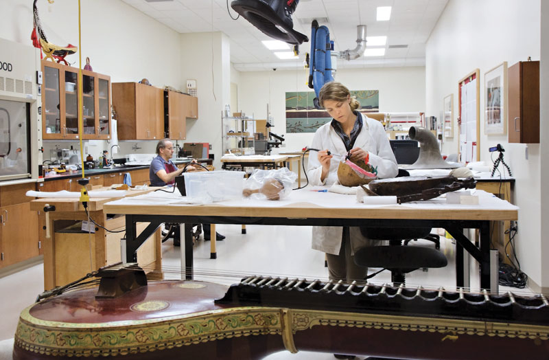 Conservator Rachel Waters works on repairing a 19th-Century African fiddle in the Musical Instrument Museum's Conservation Laboratory. Visitors to the museum can watch the conservators at work through large glass windows