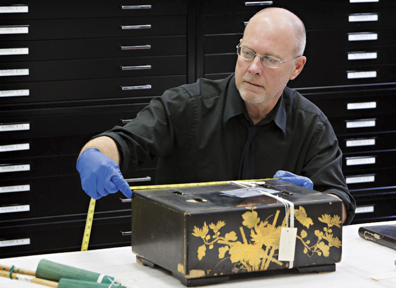 Steve Hinders, a collections tech at the Musical Instrument Museum, measures an old box from Asia before it goes into museum storage. Every item that arrives at MIM is processed &ndash; including measurements, tagging and photographing &ndash; prior to storage and display. For items that have multiple components (such as mouthpieces, cases and certificates), each part must be processed individually