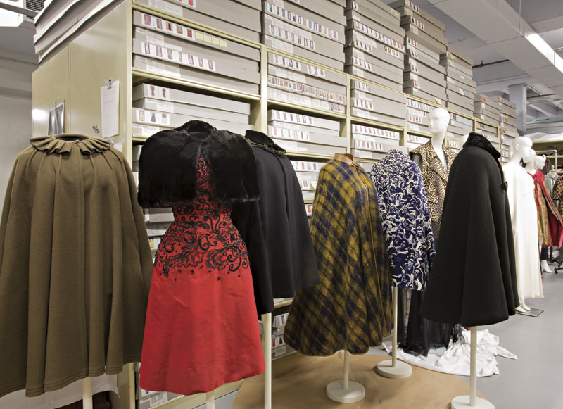 Mannequins lined the aisle in the fashion vault at Phoenix Art Museum as curator Dennita Sewell prepared for The Cape exhibit, running Sept. 15, 2013, through Feb. 9, 2014. Among the objects pulled from the collection were a 19th-century cape (far left), a plaid mohair cape (fourth from left), and a cape bearing a print of the audience at the 1969 Woodstock festival (fifth from left). Behind that is a leopard print Givenchy dress on loan from Paris