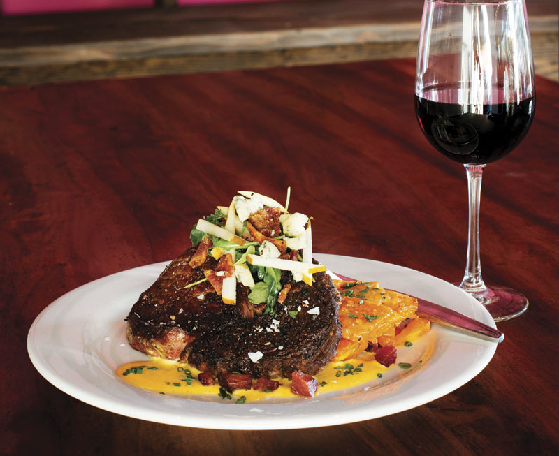 Photo by David Venezia; Cast iron rib eye with carrot gratin and bacon hollandaise, topped with a salad of arugula, pears, bleu cheese and bacon, at The Abbey Eat + Drink