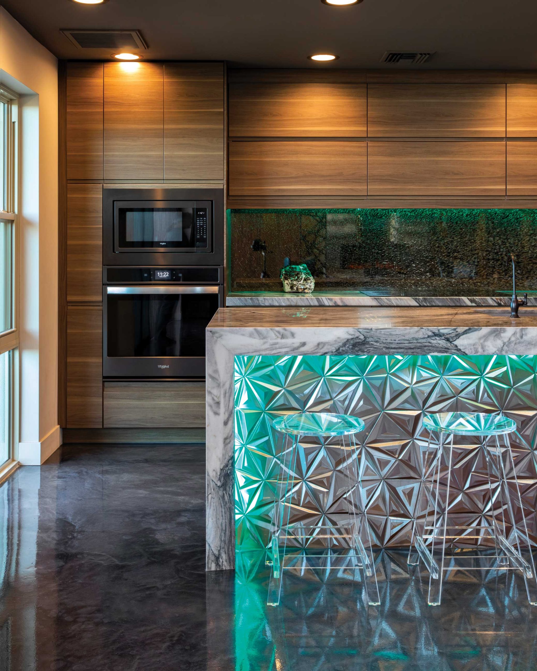 In the kitchen, hidden accent lights can change hues, and the reflective surfaces, including the crackle black backsplash and metallic tile facade on the island, follow suit. To contrast the high-shine elements, interior designer Esther Boivin chose walnut cabinetry and bluish-gray quartzite slab countertops for their earthy aesthetics. In the kitchen, hidden accent lights can change hues, and the reflective surfaces, including the crackle black backsplash and metallic tile facade on the island, follow suit. To contrast the high-shine elements, interior designer Esther Boivin chose walnut cabinetry and bluish-gray quartzite slab countertops for their earthy aesthetics.