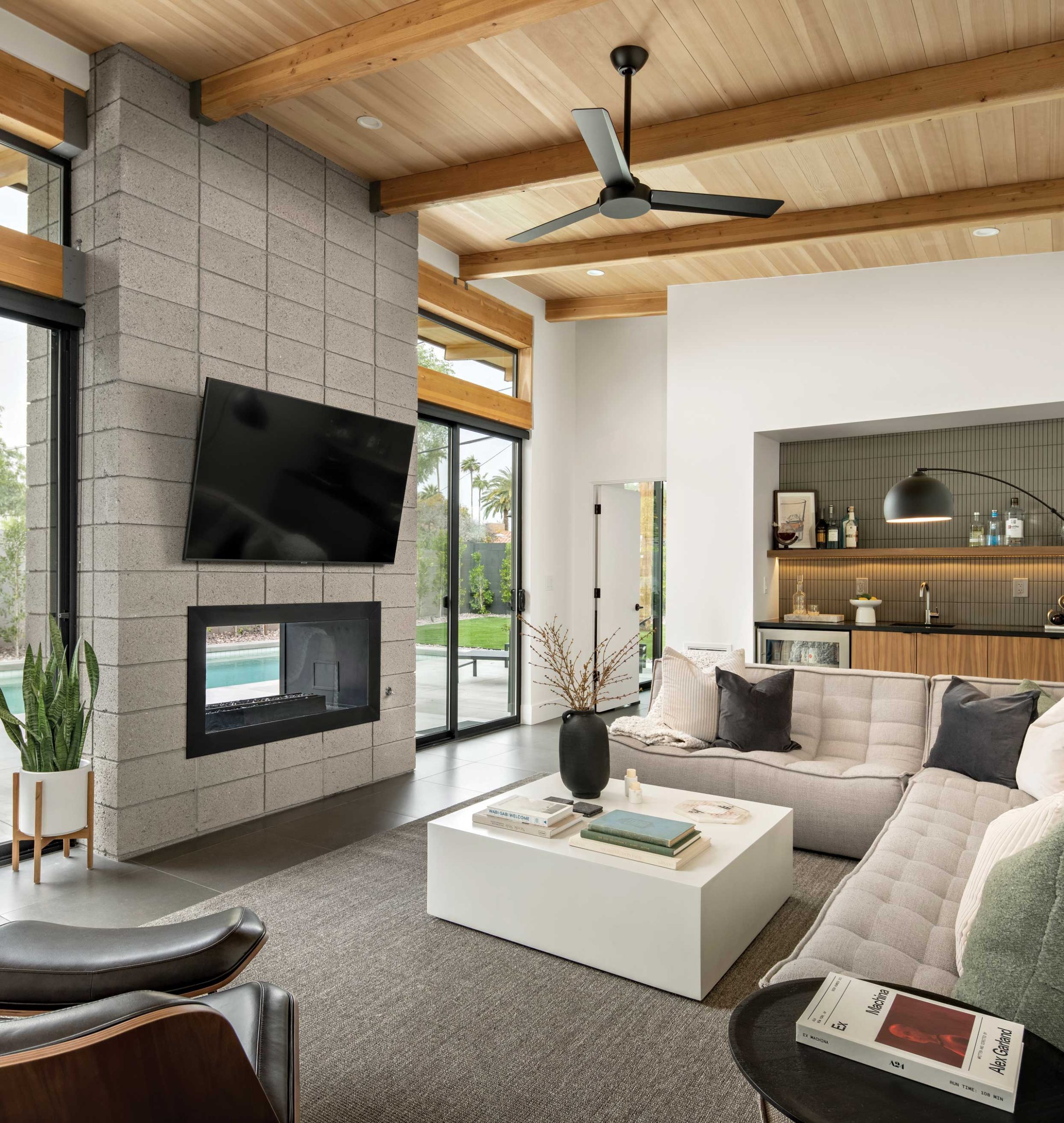 Large sliding glass doors and transom windows allow natural light to enter, while the high, slanted ceiling of exposed wood creates the coziness of a modern cabin. A floating walnut shelf with an under light adds character to the wet bar. Still more light arrives through the two-way fireplace nestled within stacked masonry, paying homage to Haver’s use of brick in the original home from 1950. Large sliding glass doors and transom windows allow natural light to enter, while the high, slanted ceiling of exposed wood creates the coziness of a modern cabin. A floating walnut shelf with an under light adds character to the wet bar. Still more light arrives through the two-way fireplace nestled within stacked masonry, paying homage to Haver’s use of brick in the original home from 1950.