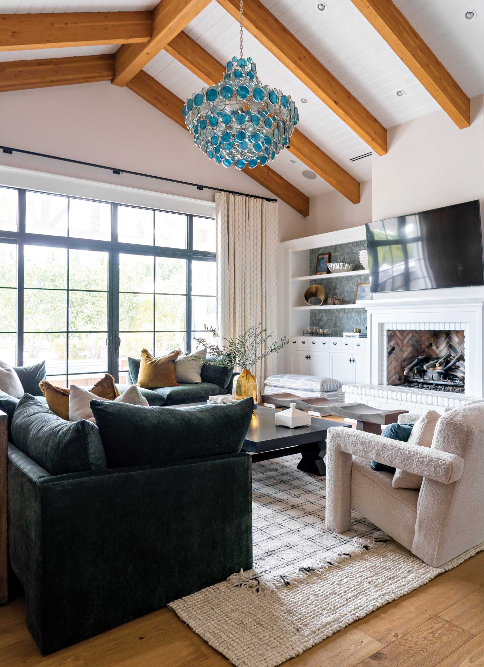 A deeply hued sectional in the great room adds heft to the soaring ceilings, as do the coffee table and the mango wood bench. The interior designer wallpapered the back of the bookcases to draw the eye to the collectibles on display. A deeply hued sectional in the great room adds heft to the soaring ceilings, as do the coffee table and the mango wood bench. The interior designer wallpapered the back of the bookcases to draw the eye to the collectibles on display.